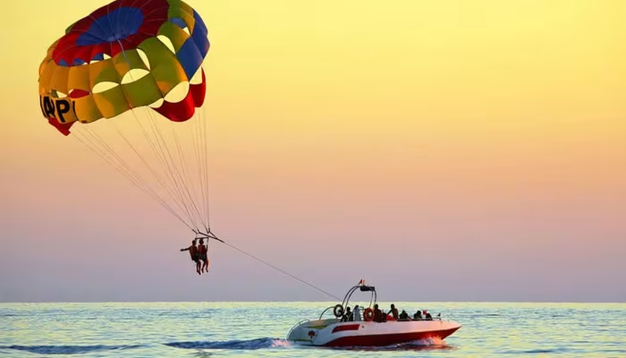 Adventure-filled tour packages featuring parasailing over the ocean, with a colorful parachute soaring above a speedboat at sunset, capturing thrill, excitement, and scenic coastal views.