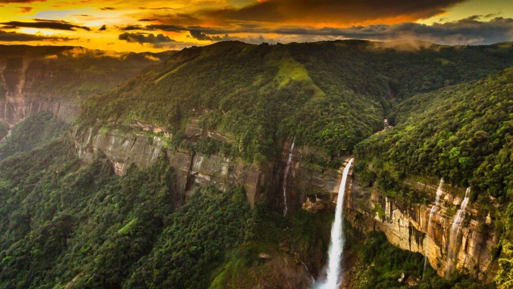 Dramatic view of towering waterfalls cascading down lush green cliffs in Cherrapunji, showcasing one of the most iconic places to visit in Meghalaya.